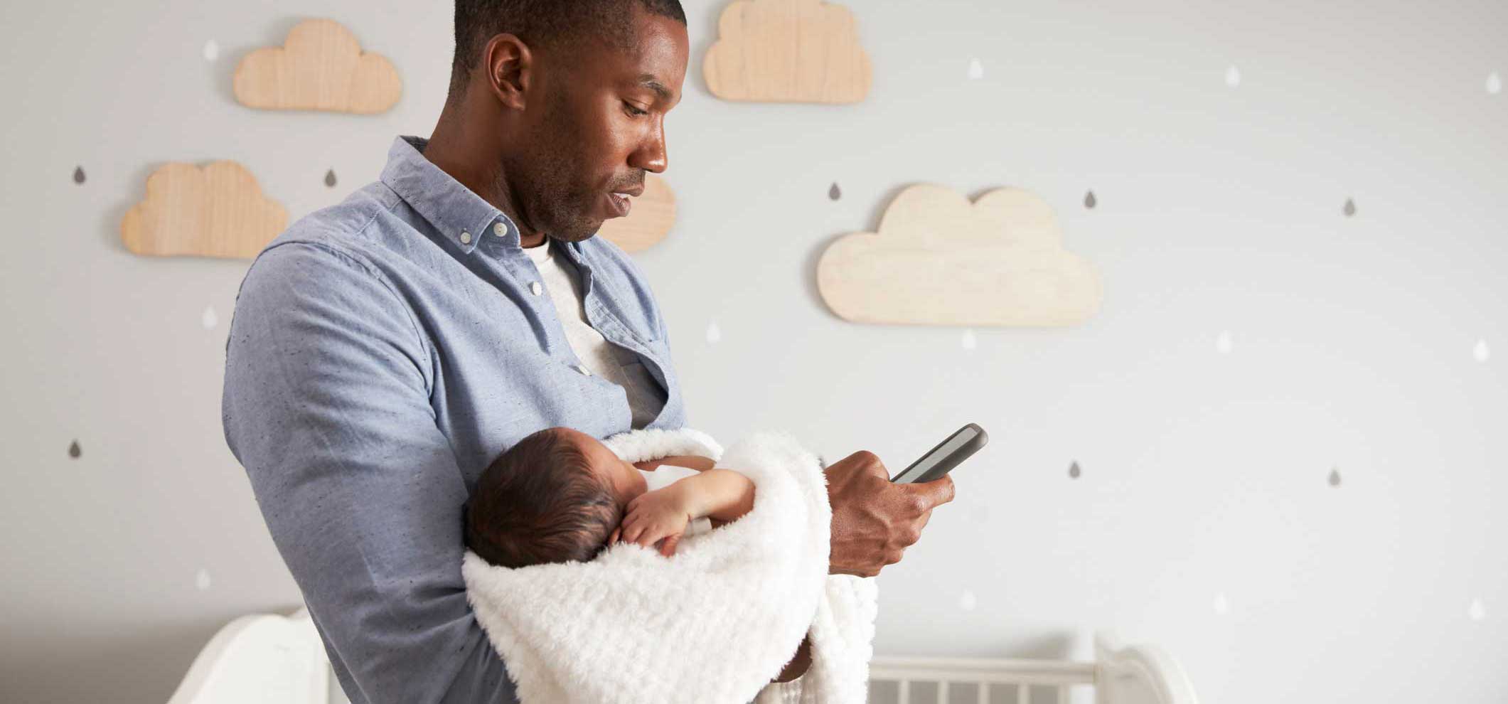 Father holding infant child while searching on mobile phone.